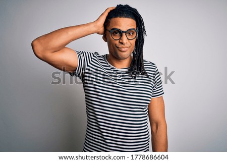 Young handsome african american man with dreadlocks wearing striped t-shirt and glasses confuse and wonder about question. Uncertain with doubt, thinking with hand on head. Pensive concept.