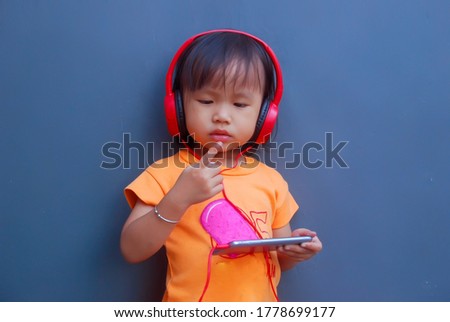 cute Asian little girl listening to music on a smartphone using a headset
