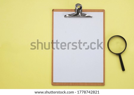 
Clipboard and white paper with a magnifying glass on a yellow background