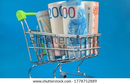 Russian rubles in a trolley on a blue background. Grocery basket and Russian rubles. World economic crisis. Selective focus.