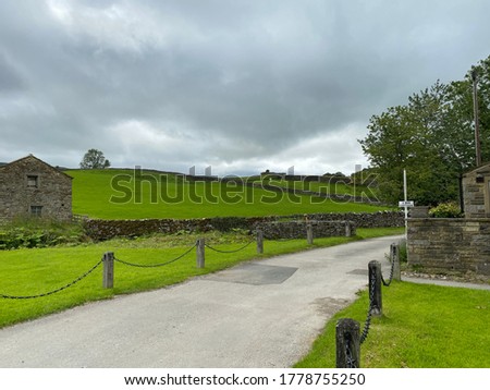 Old barn, next to a house, with a road, fencing, and heavy rain clouds near, Gargrave, Skipton, UK