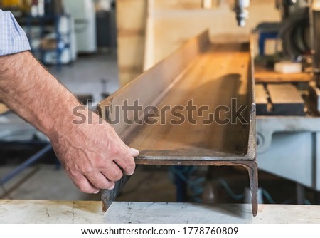 A worker in a factory holds two metal beams before drilling holes in them
