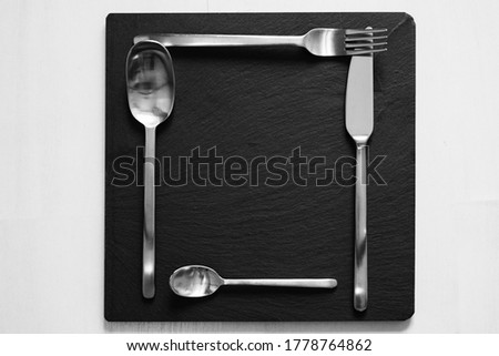 Creative image of steel cutlery placed on a square black stone kitchen plate on a white background. Royalty-Free Stock Photo #1778764862