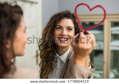 Businesswoman is drawing heart with lipstick on the mirror while preparing for work. Royalty-Free Stock Photo #1778804519