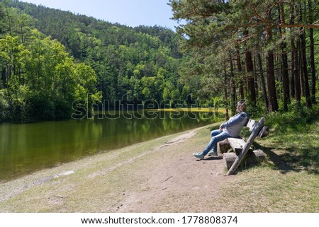 A middle-aged woman sits on a bench by the pond