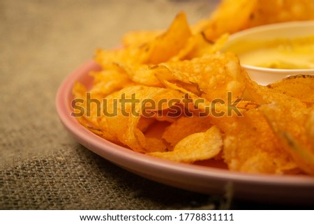 Potato chips on a round platter and a saucepan with cheese sauce. Close up.