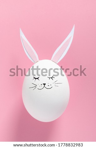 Easter egg with bunny ears and face on pink background with copy space. Flat lay. Minimal concept. Conceptual creative photo approaching Happy Easter holiday