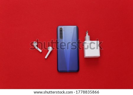 Modern gadgets. Modern smartphone with wireless earphones, charger on red background. Top view. Flat lay