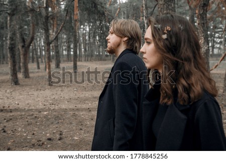 Young couple in the forest. Love story, black coat and dried flowers.