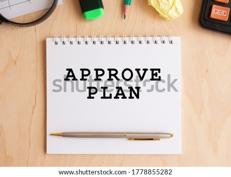 Notepad with text APPROVE PLAN on a wooden table, near calculator and office supplies. Business concept.