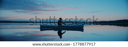 Man canoeing in a traditional wooden boat on a large lake at dawn Royalty-Free Stock Photo #1778877917