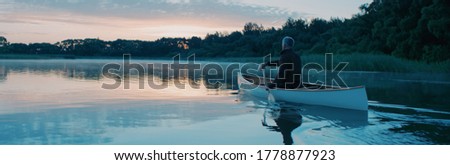Man canoeing in a traditional wooden boat on a large lake at dawn Royalty-Free Stock Photo #1778877923