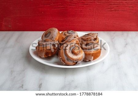 Side view of bite size cinnamon swirl rolls on a white plate atop a marble tabletop with a red wall in the background illuminated with window light. Royalty-Free Stock Photo #1778878184