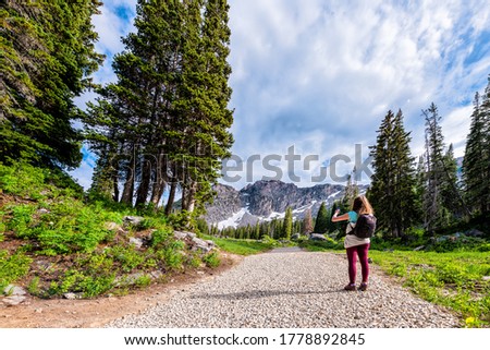 Albion Basin, Utah pine trees wide angle view and woman taking pictures on summer Cecret Lake trail in 2019 in Wasatch mountains with rocky snowy Devil's Castle mountain