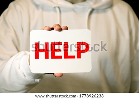 HELP, Teenager with help sign. girl holding a paper with the inscription. teenage girl in casual clothes holding sheet of paper. Girl holding sheet of paper with word HELP on grey wall background