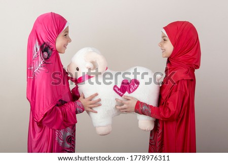 Little Muslim girl give a sheep toy to her friend as a present for Eid Al Adha - Happy Sacrifice Feast Royalty-Free Stock Photo #1778976311