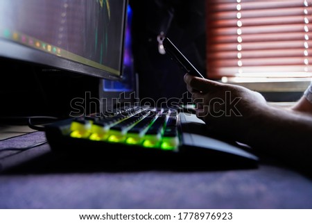 Gamer Designer Freelancer holding a mobile smart phone in front of computer