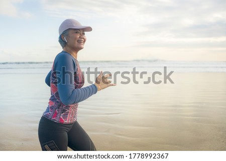 fit and happy middle aged woman running on the beach - 40s or 50s attractive mature lady with grey hair doing jogging workout enjoying fitness and healthy lifestyle at beautiful sea landscape Royalty-Free Stock Photo #1778992367