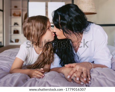 cheerful and beautiful mother and daughter together in the bedroom. Interior, family, love, support, kiss, mom and daughter concept. 