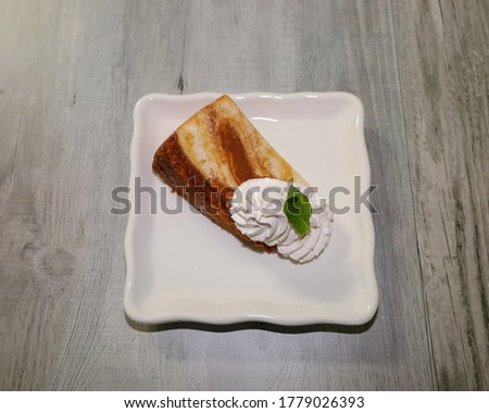 A piece of cheesecake on a white sprinkled with cinnamon sugar and topped with whipped cream.