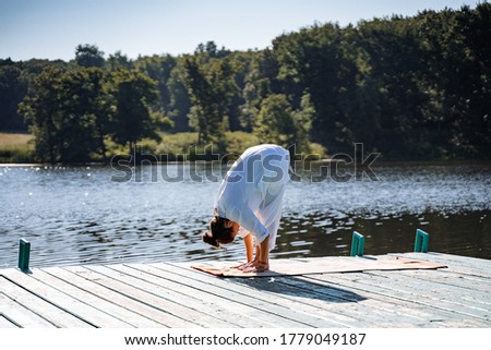 a young girl in white clothes does yoga on a pier on a summer Sunny day, yoga asana pose, morning gymnastics, outdoor fitness, sun salute complex