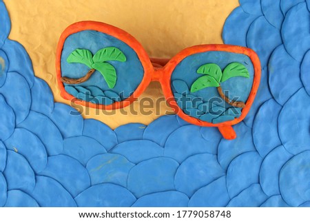 Sunglasses and sea coast made of plasticine, top view. Sunglasses with reflection of sea and palms.  Holiday concept. Sea, sand and beach concept.
