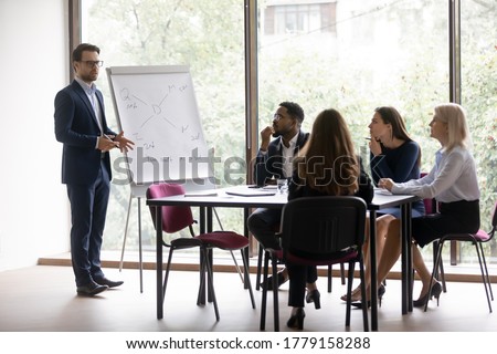 Businessman in suit standing near flip chart in front of interested collective provide information do overview sales result, make presentation for investors, plan common project, coaching work concept Royalty-Free Stock Photo #1779158288