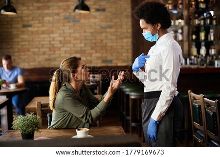 Dissatisfied female customer discussing with African American waitress in a pub. 