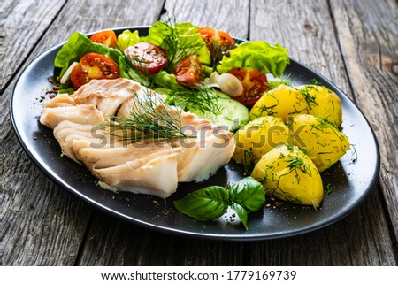 Fish dish - fried cod fillet with vegetables on wooden table 
