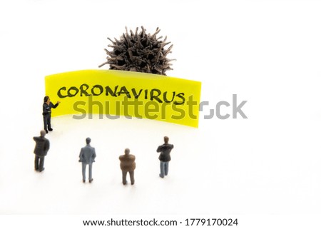 Meeting with miniature figurines posed as business people standing around post-it note with Coronavirus handwritten message in background, minimalist abstract concept with focus on text