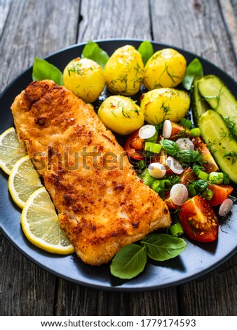 Fish dish - fried breaded cod fillet with vegetables on wooden table 