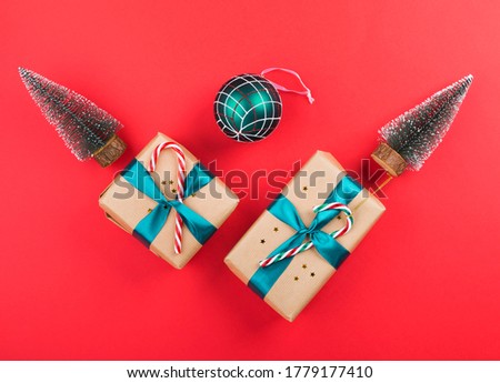 Christmas new year gift boxes wrapped in craft paper with green ribbon and candy canes on red. Festive flat lay background with toy xmas trees
