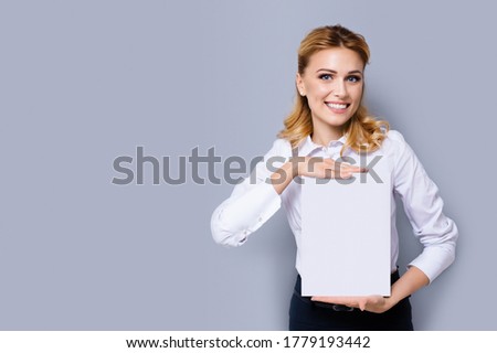 Happy smiling businesswoman in white confident style clothing showing blank paper signboard. Success in business concept. Copy space empty place for some text or imaginary. Grey background.