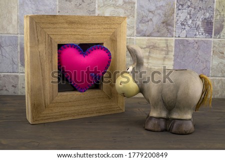 Cute little toy donkey look at handcrafted pink heart in a wooden frame against a tiled background