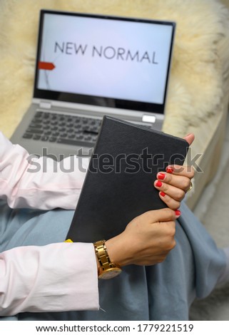 view of woman's hands working in the new normal behavior work from home, using pink blazer and rose gold watch, holding her notebook and ready for doing some work in her laptop
