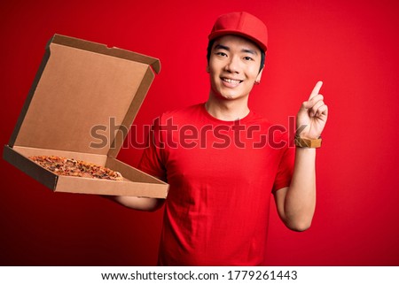 Young handsome chinese delivery man holding deliver box with delicious Italian pizza surprised with an idea or question pointing finger with happy face, number one