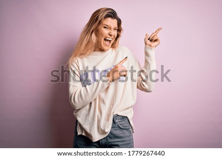 Young beautiful blonde woman wearing casual sweater standing over pink background smiling and looking at the camera pointing with two hands and fingers to the side.