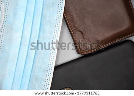 Close-up photo of triangle formed by surgical mask, leather wallet and mobile phone on gray background.