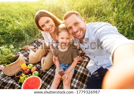 Vacation Concept. Top view of family taking selfie, sitting on the blanket in the countryside on a sunny day