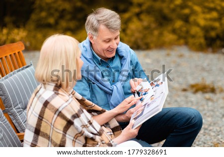 Elderly man with his beloved wife looking at photos in family album during summer vacation outdoors