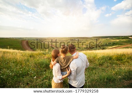 Parenthood Concept. Rear view portrait of happy family holding kid on hands, standing in the middle of the field