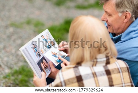 Sharing happy memories. Senior man with his wife leafing through photo album outdoors, panorama