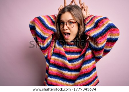 Young beautiful blonde girl wearing glasses and casual sweater over pink isolated background Posing funny and crazy with fingers on head as bunny ears, smiling cheerful