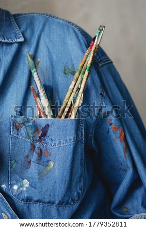 Close up of paint brushes and palette knife placed in the pocket of a denim shirt.