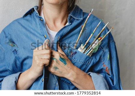 Cropped image of woman with paint brushes and palette knife placed in the pocket of her denim shirt.