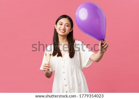 Celebration, party holidays and fun concept. Tender pretty asian woman in white dress, holding balloon and glass champagne, making toast during event, congratulating hosts, pink background