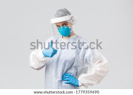 Covid-19, preventing virus, health, healthcare workers and quarantine concept. Confident serious doctor in personal protective equipment, female nurse show thumb-up, fighting coronavirus
