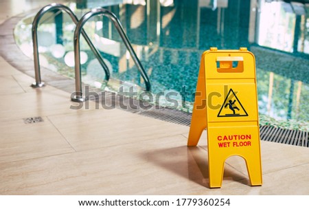 Yellow sign of wet floor plate is near the swimming pool.