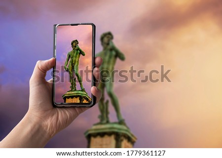 Tourist taking photo of replica of Michelangelo's David statue in Michelangelo Square during sunset in Florence, Italy. Man holding phone and taking picture.