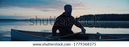 Portrait of mid 50s man canoeing alone boat on a large lake at dawn Royalty-Free Stock Photo #1779368375